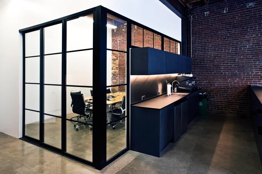 Modern office kitchenette adjacent to a glass-walled conference room featuring interior glass doors.