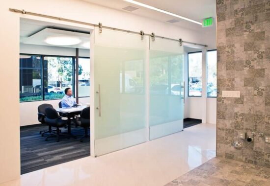 A modern office space with a person working at a desk behind interior glass barn sliding doors.