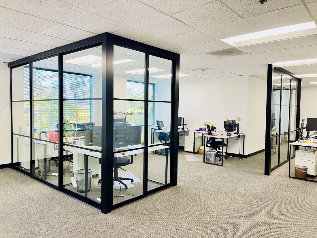 Modern office space with glass-walled cubicles, interior doors, and computer workstations.
