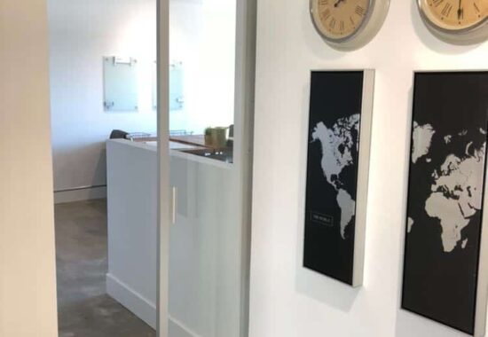 A modern office space with interior glass pocket doors, wall-mounted world map art, and a series of clocks displaying different time zones.