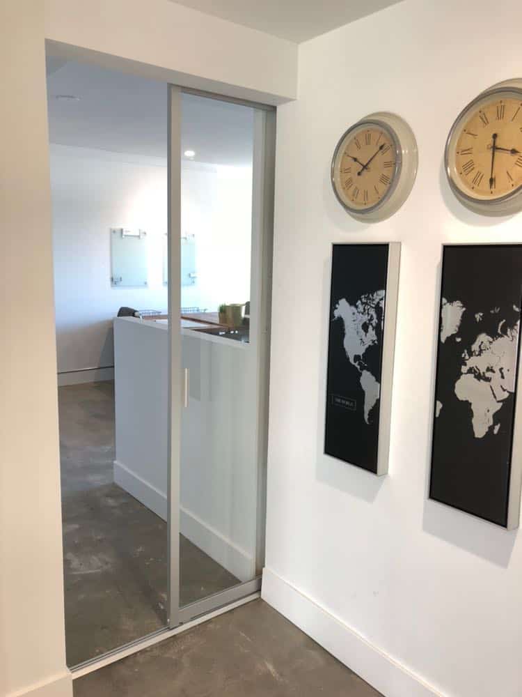Modern office interior with sliding glass pocket doors, world map artwork, and multiple time zone clocks on the wall.