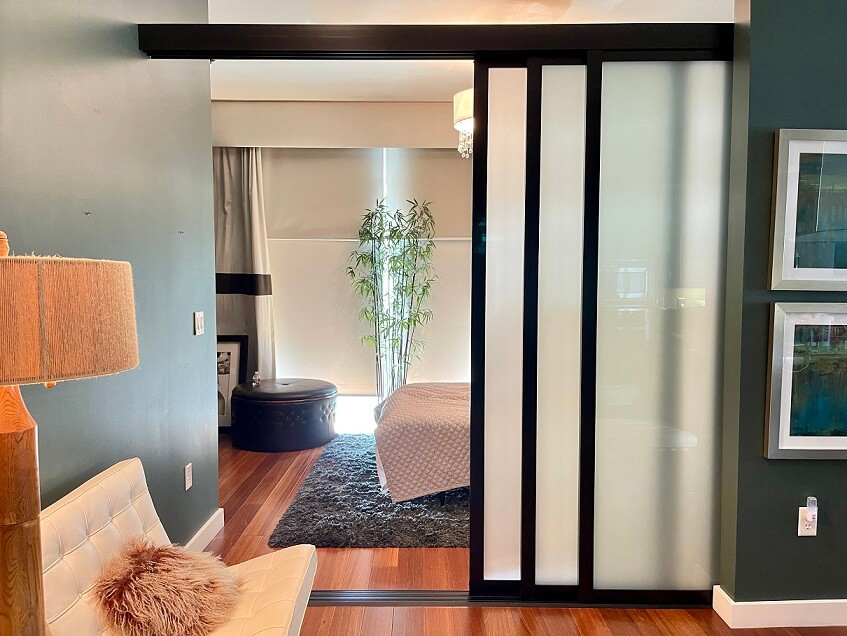 Modern bedroom viewed through sliding frosted glass doors serving as room dividers, with a contrasting dark and neutral color palette.