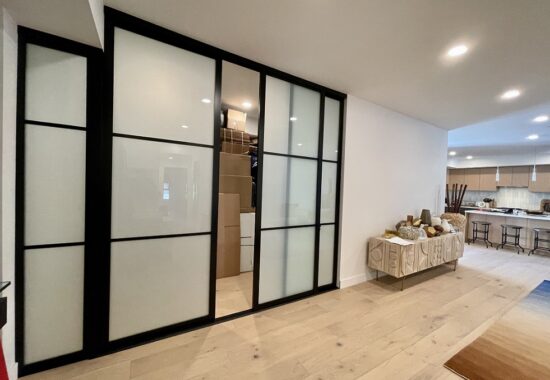 A modern interior with sliding glass interior doors separating a room from a kitchen and dining area with light wood flooring.