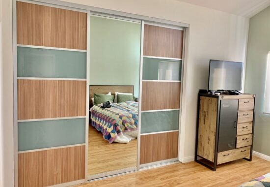 Modern bedroom with sliding glass wardrobe doors revealing a glimpse of the bed and colorful bedding.