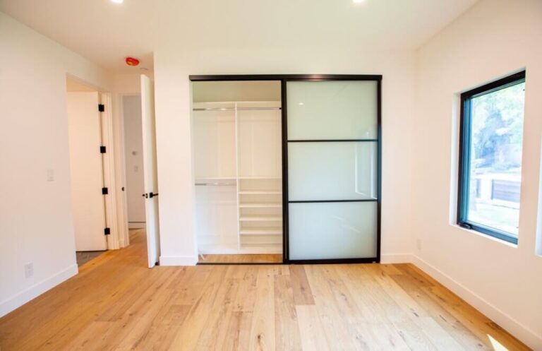 Modern empty room with hardwood floors, a frosted glass sliding door closet, and a window featuring interior doors.