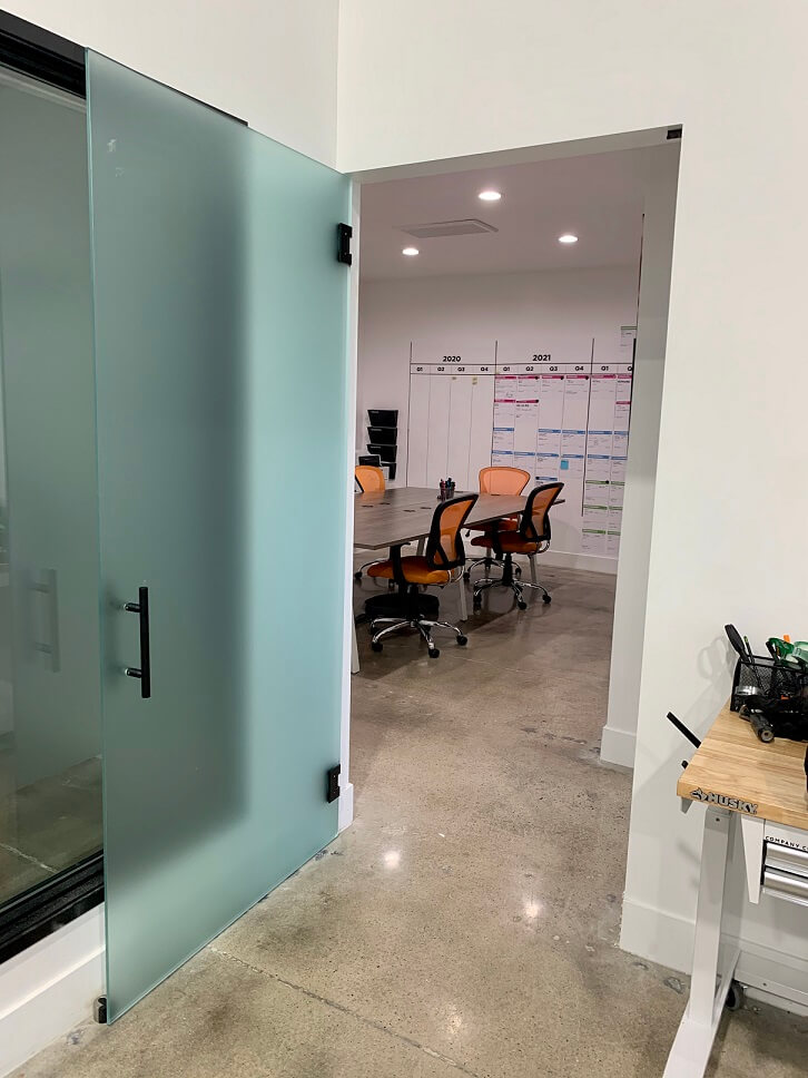 Open glass doors leading to a modern office with chairs and a whiteboard.