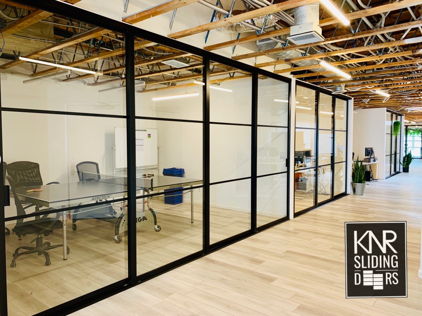 Modern office space featuring a glass-walled conference room with exposed ceiling beams and sleek glass interior doors.