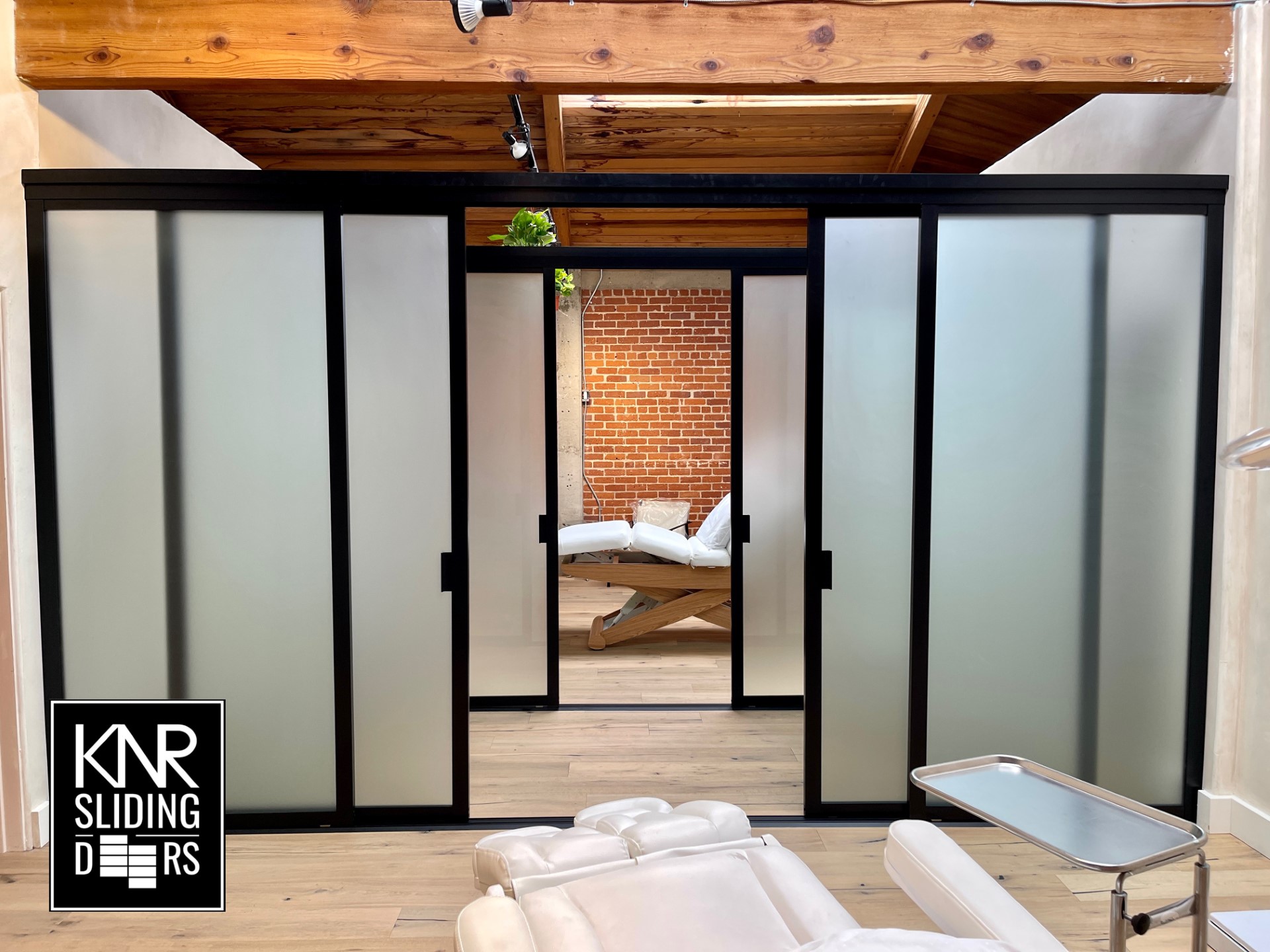 A modern room with a frosted glass sliding room divider leading to a bedroom with exposed brick walls.