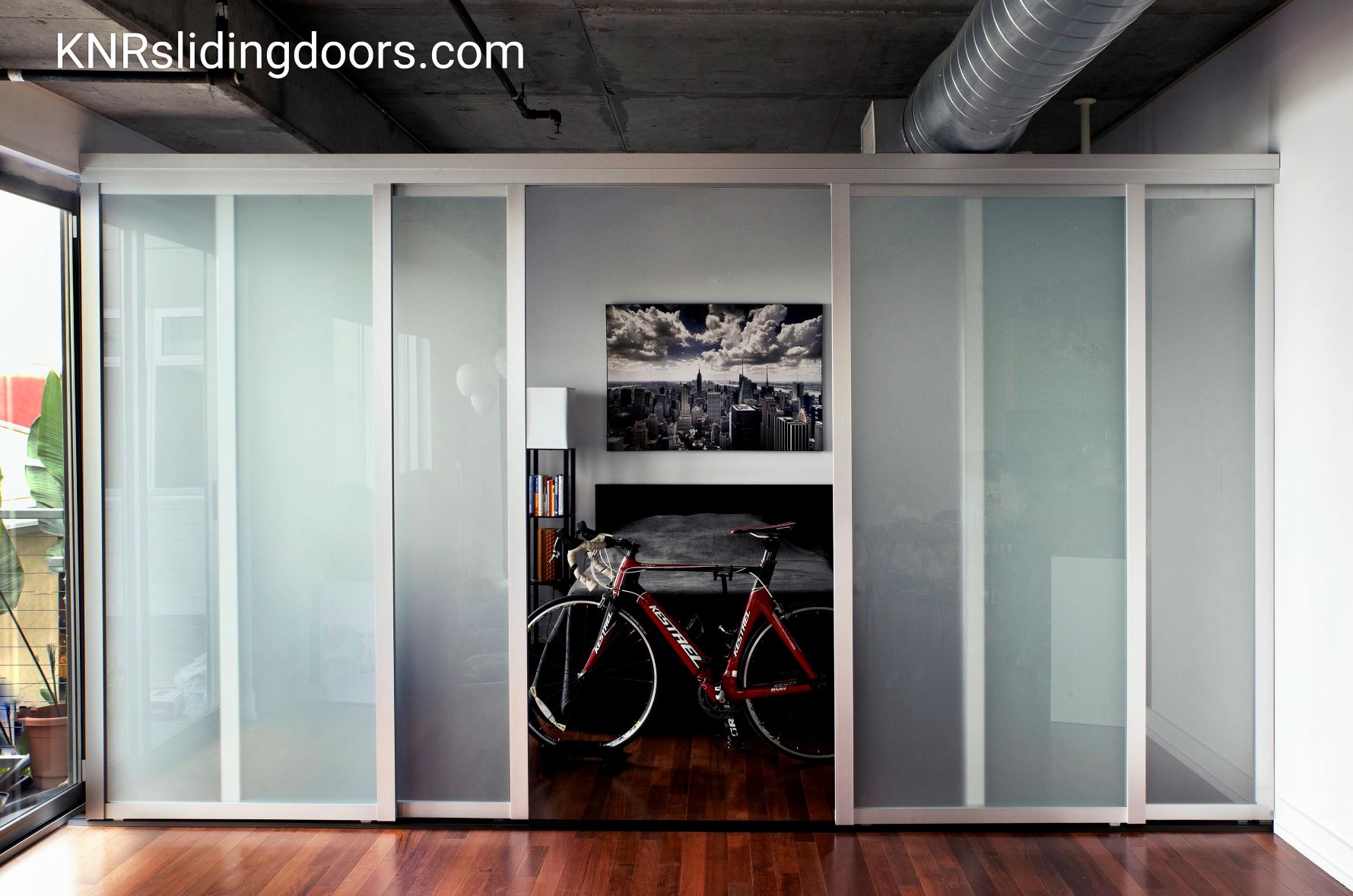 Modern interior with sliding glass doors partially revealing a bedroom and a bicycle in the foreground.