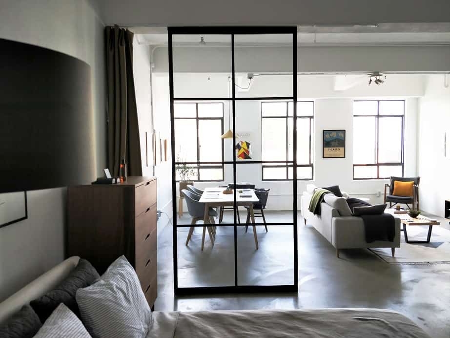 Modern studio apartment with a view into the living area from the bedroom through a large glass fix panel.