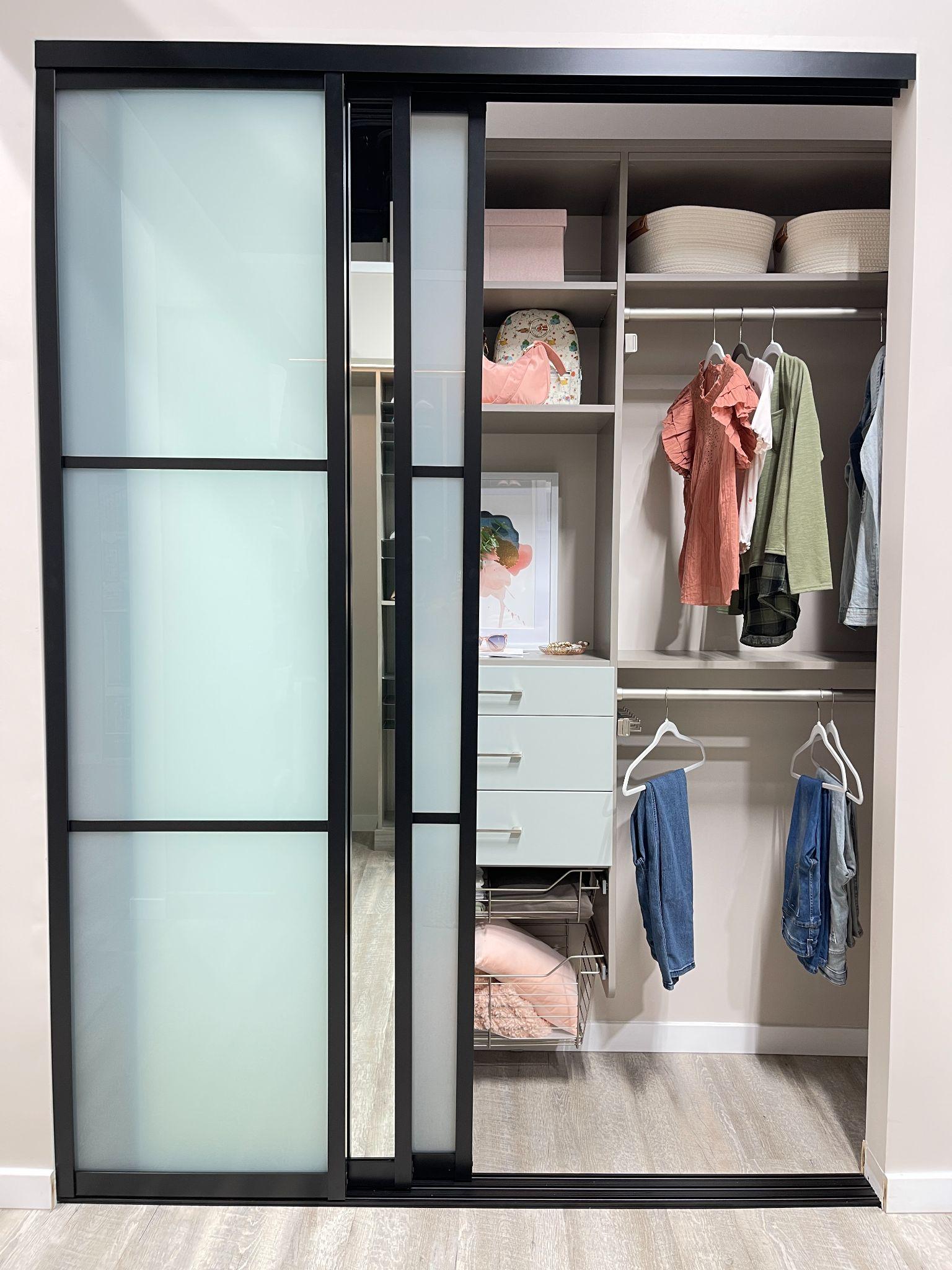 A sliding glass closet door with frosted panes half open to reveal an interior closet organizer