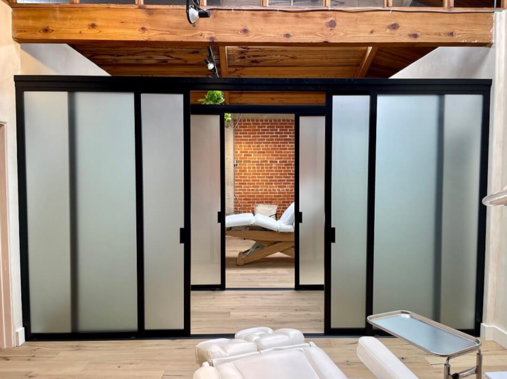 Frosted glass sliding doors with black frames in a modern interior serve as a sleek room divider, revealing a cozy seating area against a brick wall.